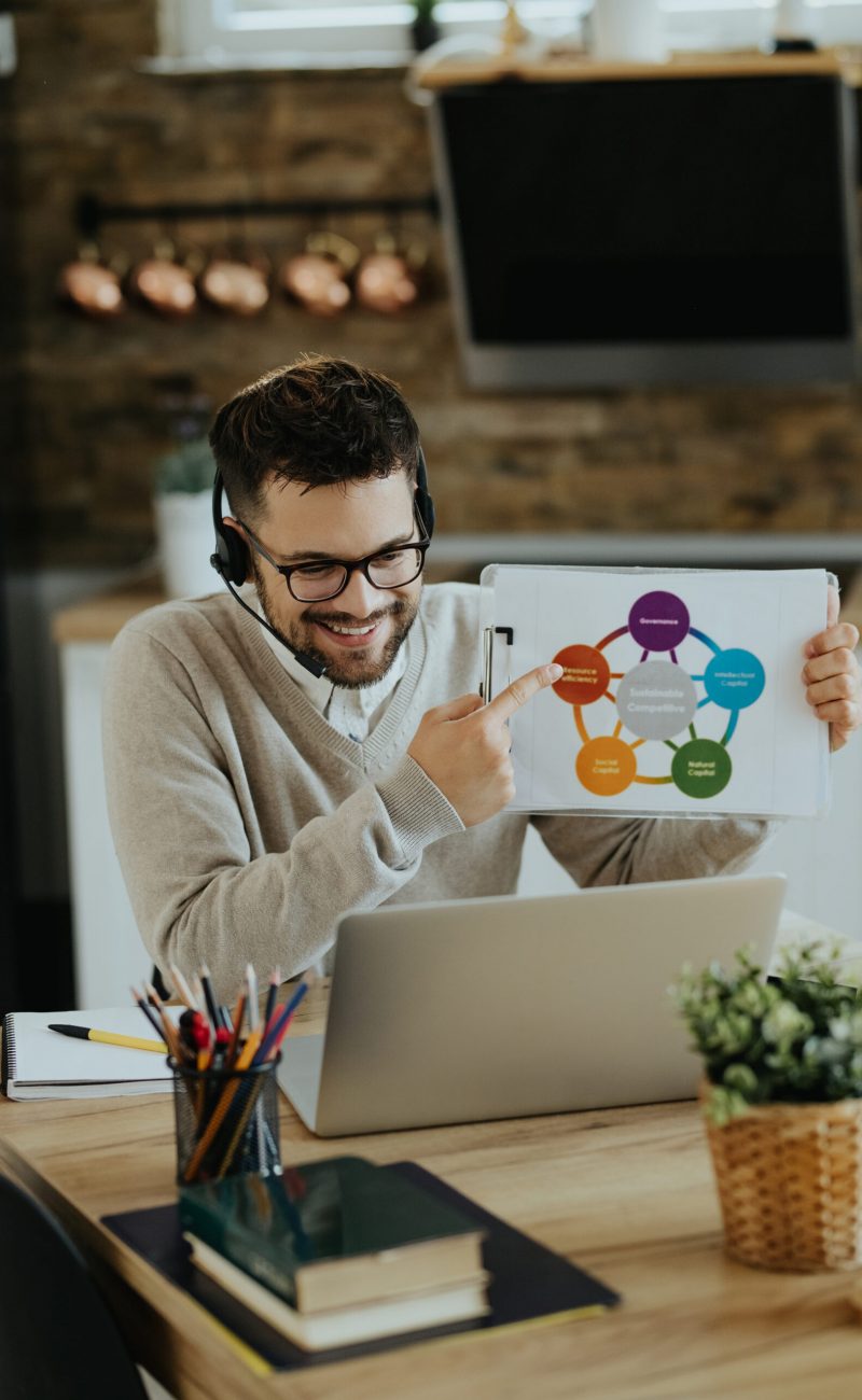 Young happy businessman examining diagram while having virtual meeting over laptop at home.